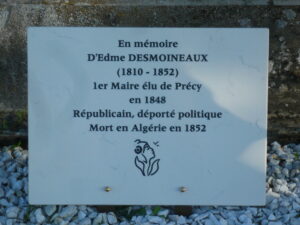 Marble memorial plaque with French text honoring Edme Desmoineaux (1810–1852) and a small flower illustration, set on a stone wall with gravel around it.