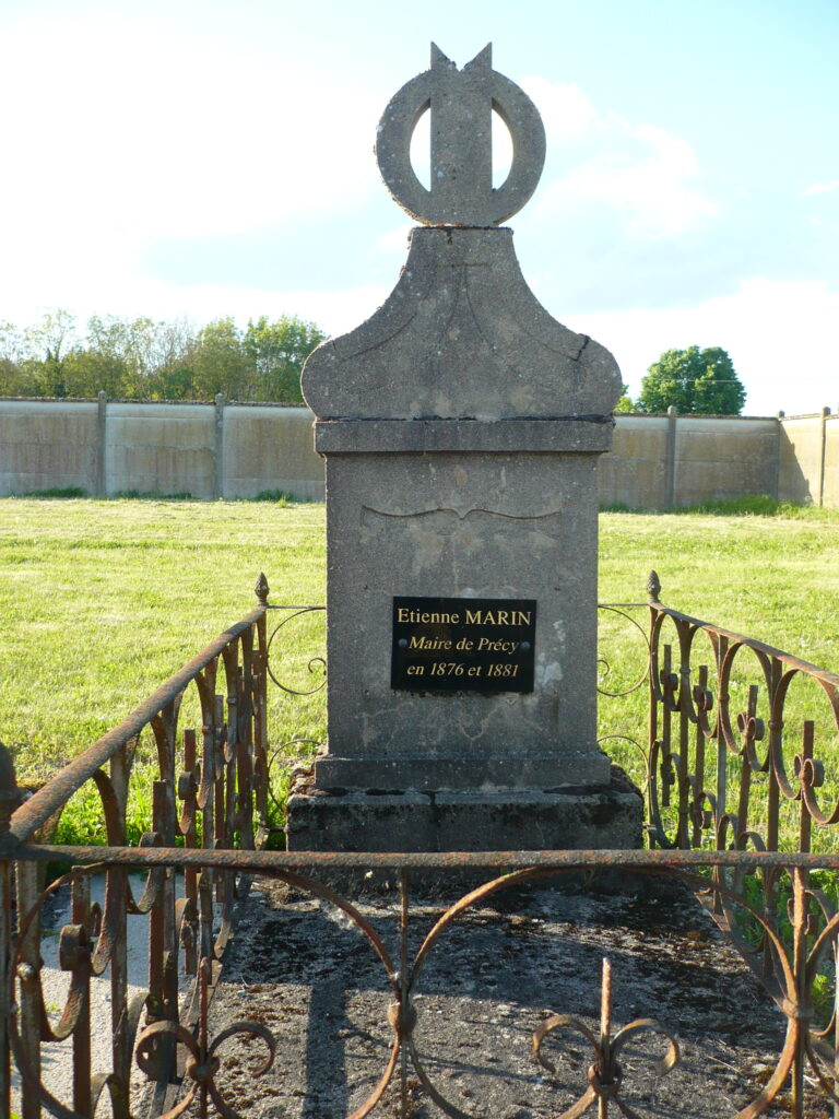 Stone grave marker with decorative top and iron railing in a grassy cemetery; plaque reads 'Etienne MARIN Maire de Précy en 1876 et 1881'