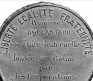 Close-up of a circular metal medallion with raised French text, including 'LIBERTÉ ÉGALITÉ FRATERNITÉ' and 'BOULANGERIE'